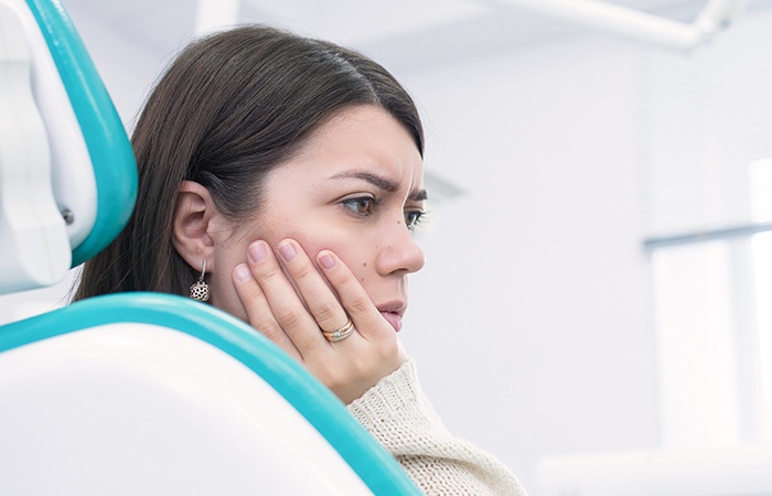Woman holding cheek in dental chair
