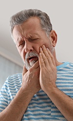 Man in striped shirt rubbing his jaw in pain