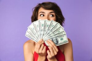 Smiling woman holding money in front of her face